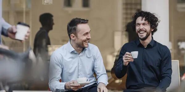 Two men laughing enjoying espressos outside