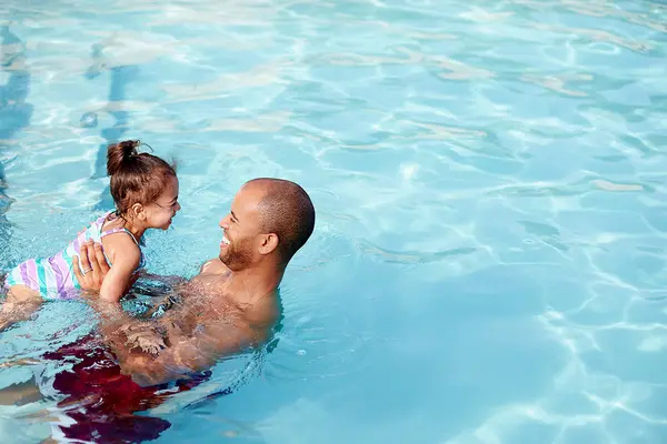 Smiling father teaching daughter how to swim in pool