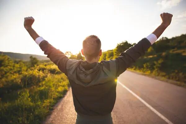  Sport and life achievements and success concept. Sporty man raising arms towards beautiful sunset on the road